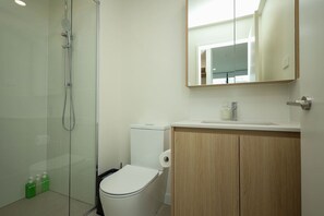Un baño moderno con cabina de ducha de vidrio, inodoro y tocador de madera con espejo.