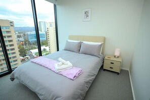 Habitación de hotel con una cama grande, una mesita de noche, una lámpara y vistas a la ciudad.