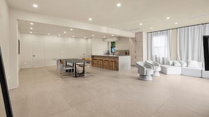Amplia sala de estar con una mesa de comedor, taburetes de bar, un sofá y una zona de cocina con barra.