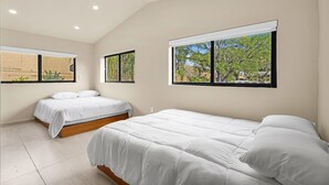 Un dormitorio con dos camas, ventanas amplias y vistas a árboles.