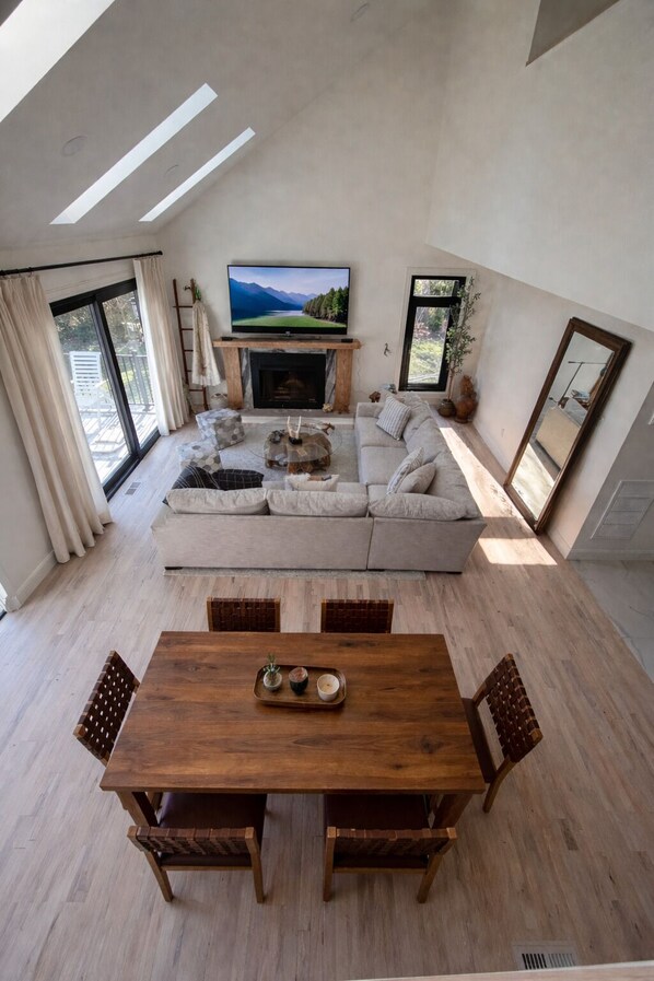 A modern living room with a fireplace, a large flat-screen TV, a sofa, and a dining table with chairs.