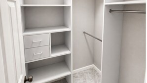 Um closet amplo com prateleiras abertas, barra de metal e porta com luminária redonda.