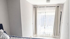 Um quarto com uma cama, uma janela com cortinas e uma luminária no teto.