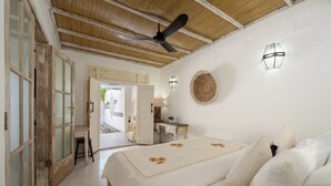 Un dormitorio con cama, escritorio, silla, ventilador de techo y puerta que da a otra habitación.