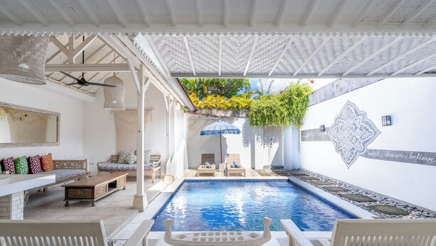 Zona de piscina con ventilador de techo, sillas de descanso y un barco decorativo en primer plano.