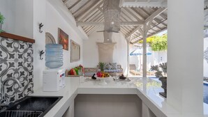 Una cocina con encimera blanca, dispensador de agua, lavamanos y comedor con mesa y sillas.