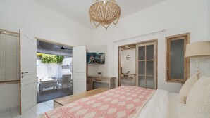 Un dormitorio con cama, escritorio, silla, planta colgante y una puerta que da a otra habitación.
