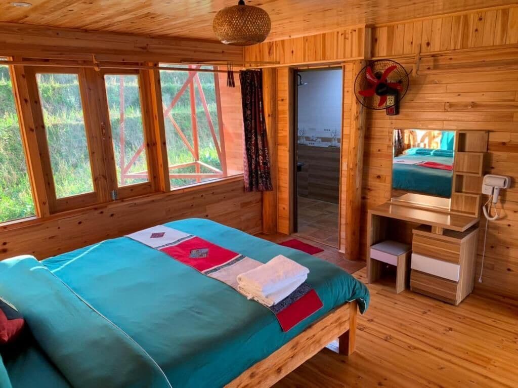 A wooden cabin room with a bed, a desk, and a window.