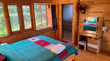 A wooden cabin room with a bed, a desk, and a window.