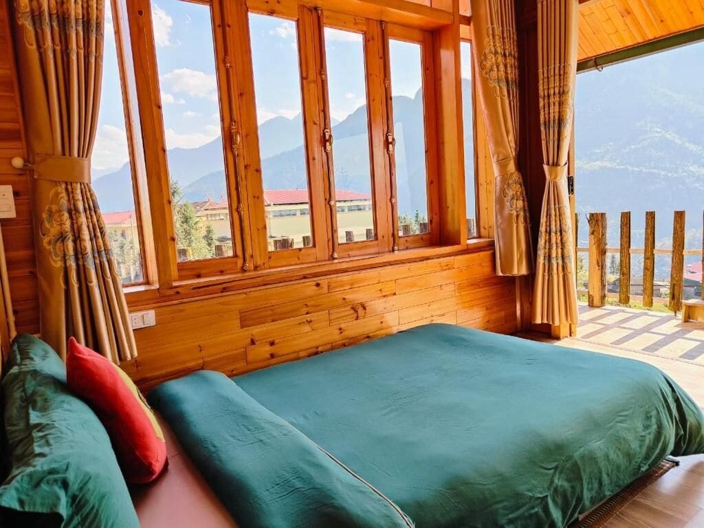 A wooden room with a bed, curtains, and a view of mountains.