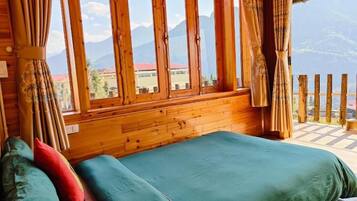 A wooden room with a bed, curtains, and a view of mountains.