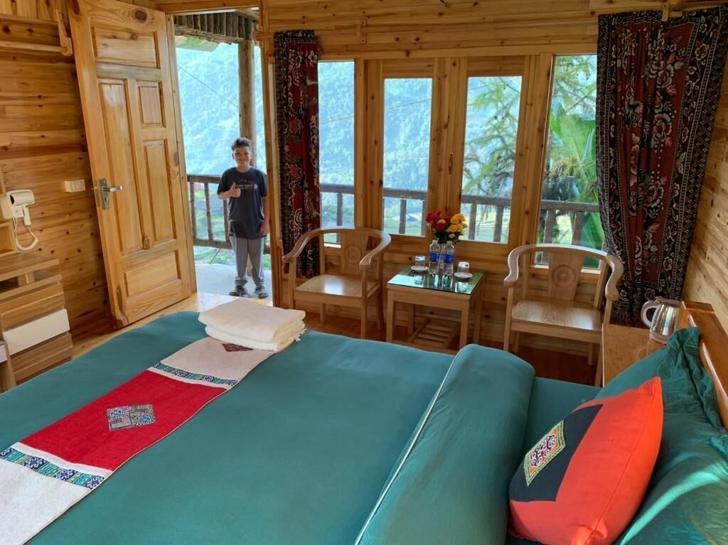 A wooden cabin with a bed, a table with chairs, and a window with curtains.