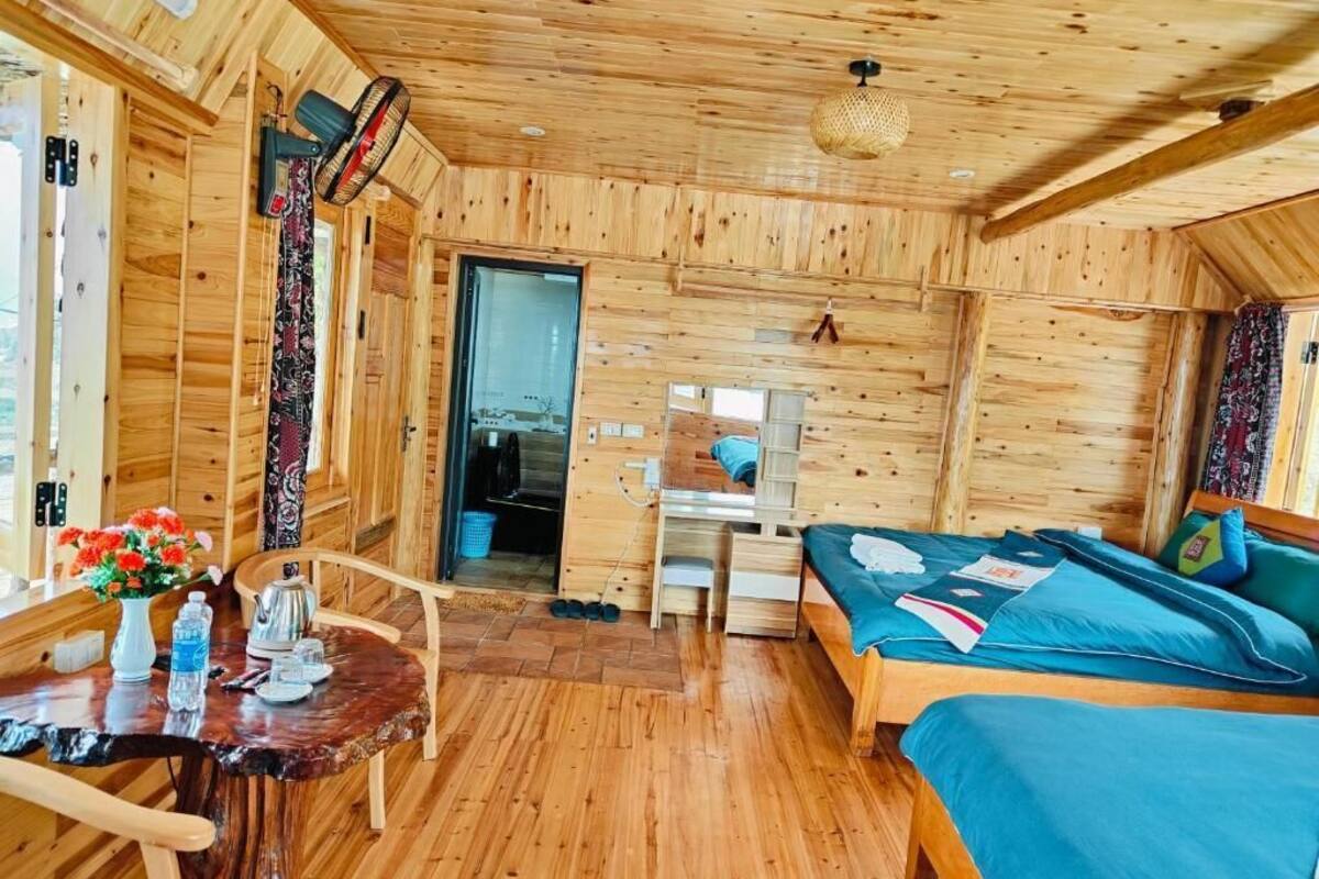 A wooden cabin interior with a bed, desk, and a small table with a vase of flowers.