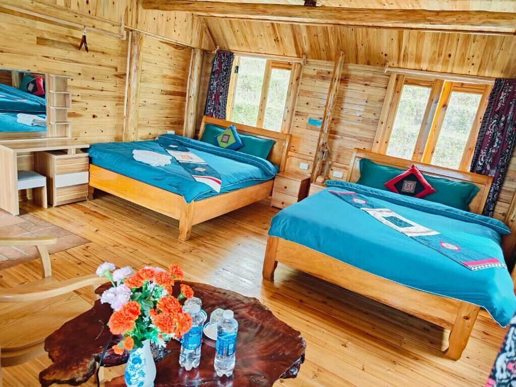 Eine Holzhütte mit zwei Betten, einem Schreibtisch und einem Couchtisch mit Blumen und Wasserflaschen.
