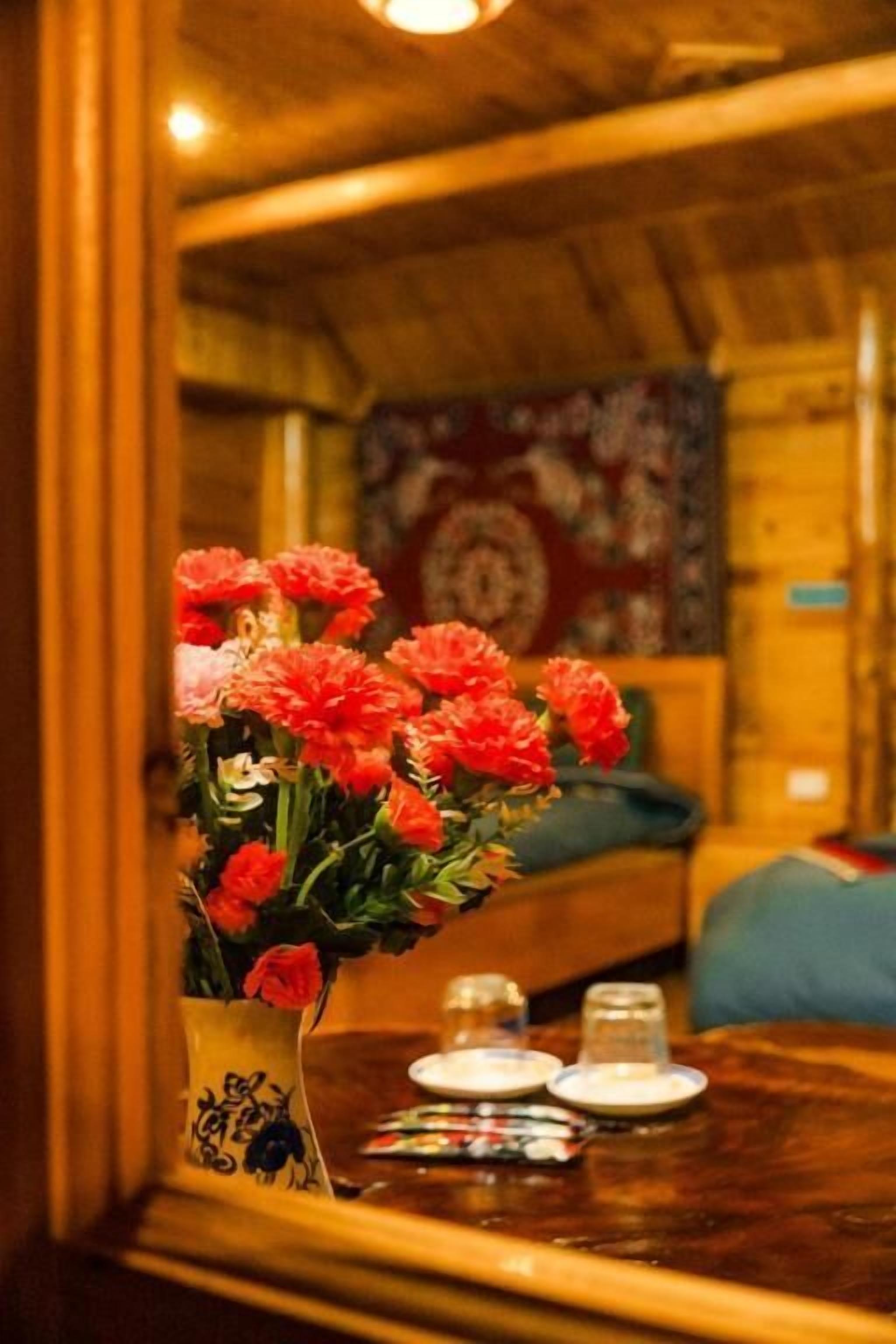 Un intérieur en bois, agrémenté d'un vase de fleurs rouges posé sur une table, d'un miroir qui reflète la pièce et d'un mur orné de motifs.