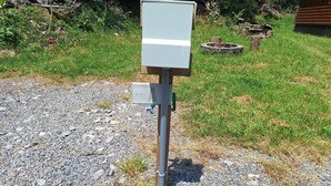 A utility box on a gravel surface with grass and a wooden structure in the background. -  camp site in charming Glenville perfect for nature lovers. (Glenville)