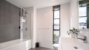 Een moderne badkamer met douche, toilet en wastafel, met een glazen douchecabine en een potplant.