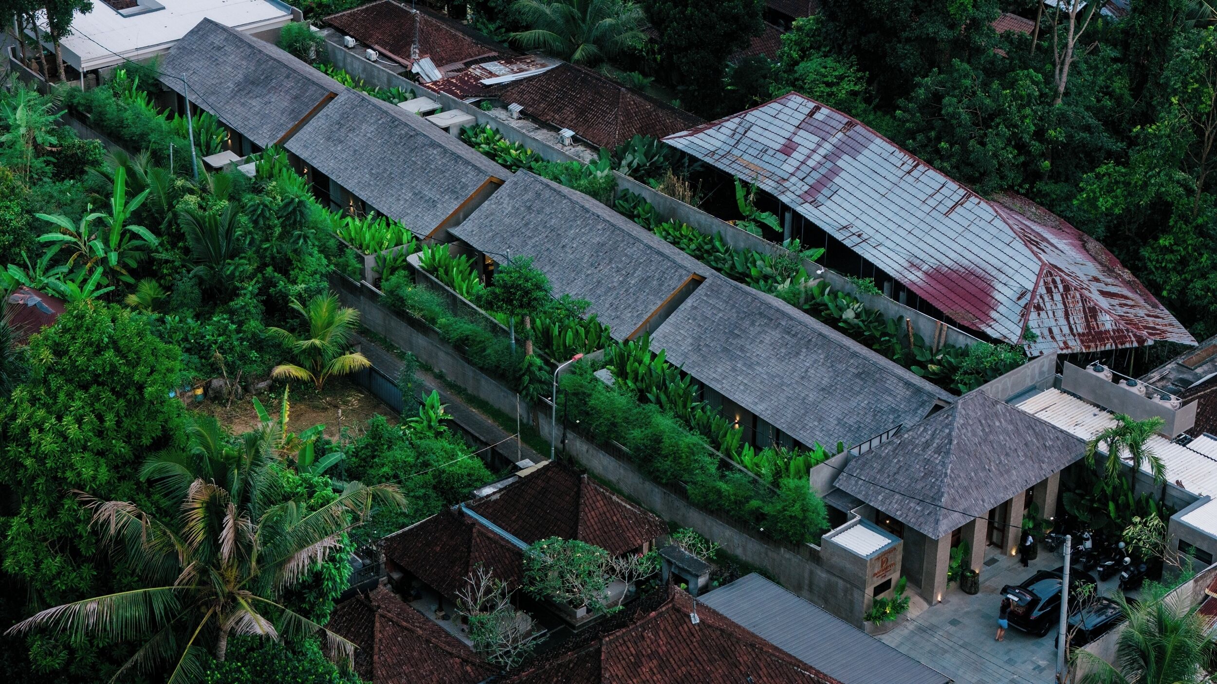 An aerial view of a traditional building with a long, narrow structure, surrounded by lush greenery and a mix of modern and traditional architecture.