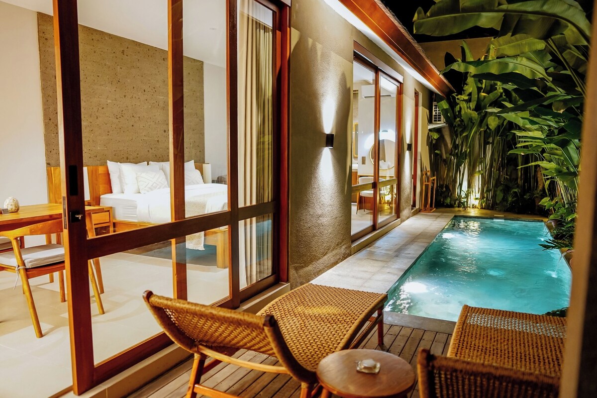 Habitación de hotel con piscina, muebles de madera y ventanas amplias.