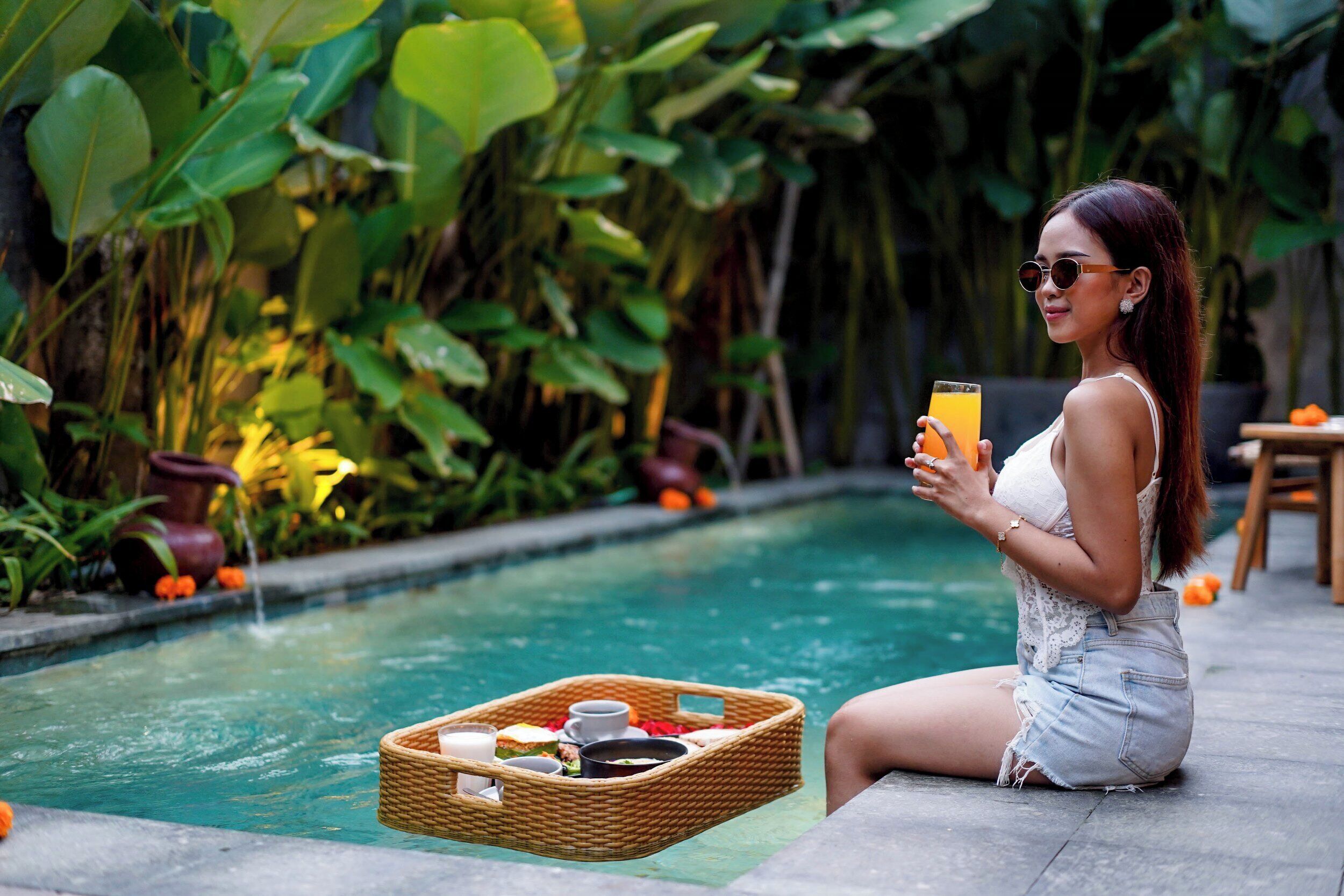 A woman sitting by a pool with a drink and a basket of food.