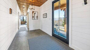 A hallway with white walls, a wooden ceiling, and a black-framed glass door leading outside. - Gray Ghost | Hot Tub | Views | Pet Friendly (Rangeley)