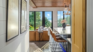 A modern kitchen with a wooden ceiling, large windows, and a dining area with a white table and brown chairs. - Gray Ghost | Hot Tub | Views | Pet Friendly (Rangeley)