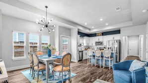 A spacious kitchen with white cabinets, a dining area with a blue sofa, and a chandelier. - 3-bedroom house with fenced yard and private pool (Pensacola)
