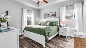 A bedroom with a bed, a nightstand, a lamp, a ceiling fan, and a window with curtains. - 3-bedroom house with fenced yard and private pool (Pensacola)