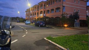Un edificio de varios pisos con balcones, un estacionamiento y una calle con coches y una motocicleta.
