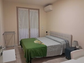 Ein Schlafzimmer mit einem Bett, einem Nachttisch, einer Lampe, einer Wand-Klimaanlage und einer mit Vorhängen versehenen Tür.