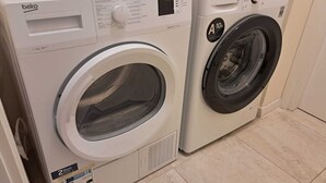 Dos lavadoras de carga frontal, una con panel blanco y la otra con panel negro, en un lavadero con piso de baldosas.