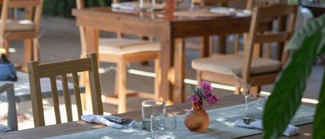 Un espace de restauration en plein air avec des tables et des chaises en bois, une nappe et un vase rempli de fleurs.