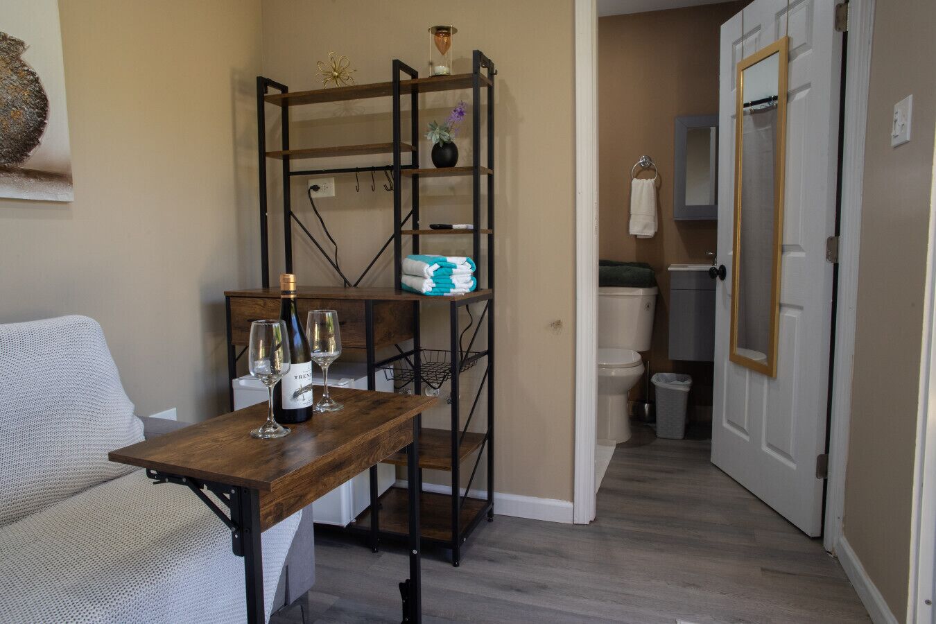 Une petite pièce comprenant une table en bois, un canapé, une étagère en métal, des toilettes et une porte.