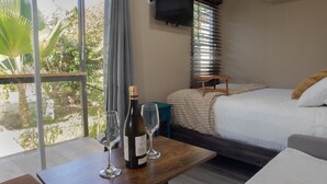 A bedroom with a bed, a bedside table with a bottle and glasses, a TV, and a window with curtains. - A unique stay steps from the beach with breakfast included (Rincón)