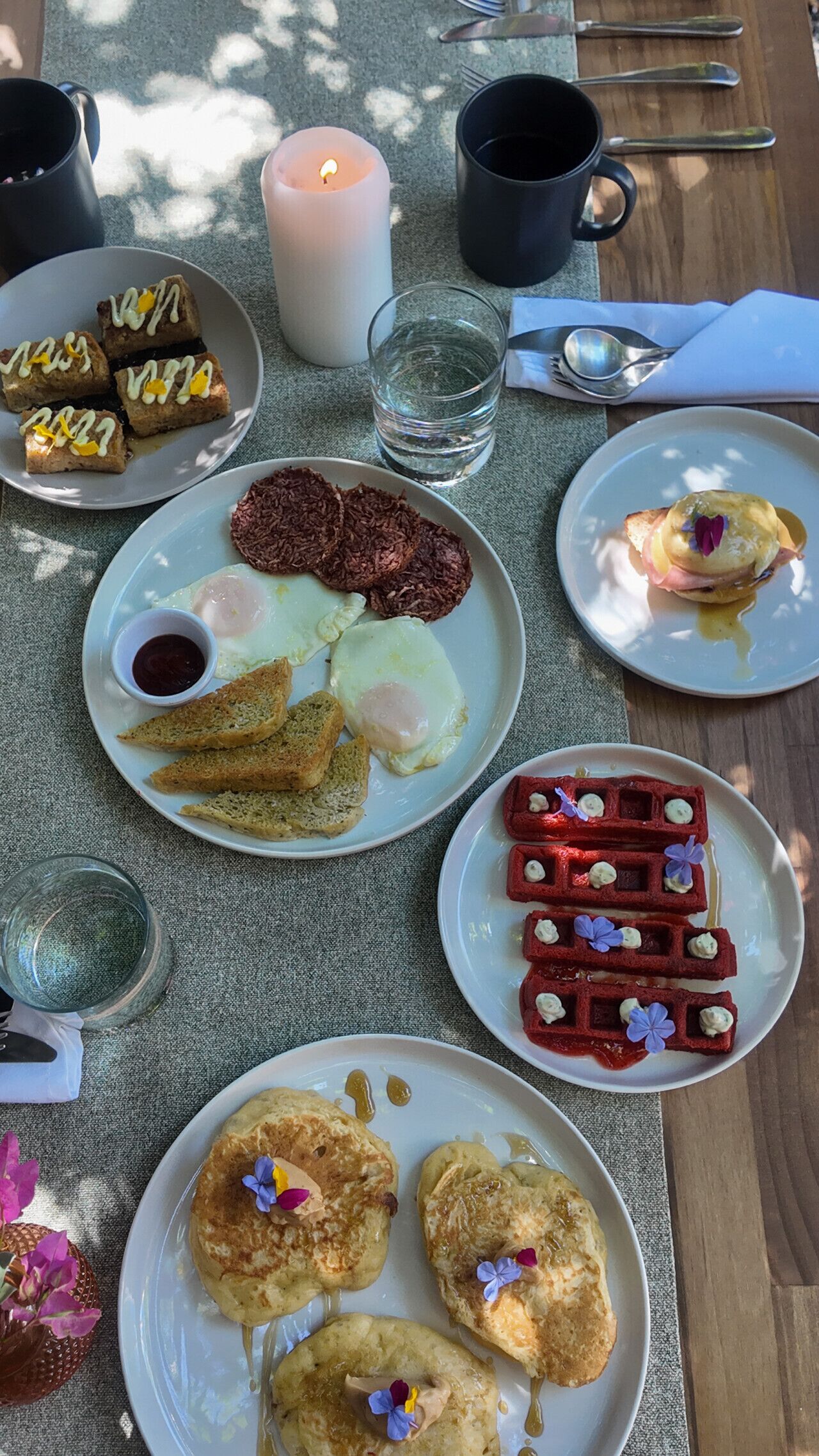 Une table mise pour le petit-déjeuner avec des assiettes d’œufs, des toasts, des gaufres et une bougie.