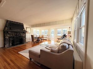 A living room with a stone fireplace, a sofa, a dining table with chairs, and large windows.