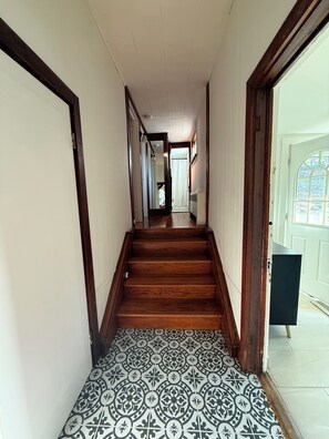 A hallway with wooden stairs, a patterned floor, and a door leading to a room with a window.