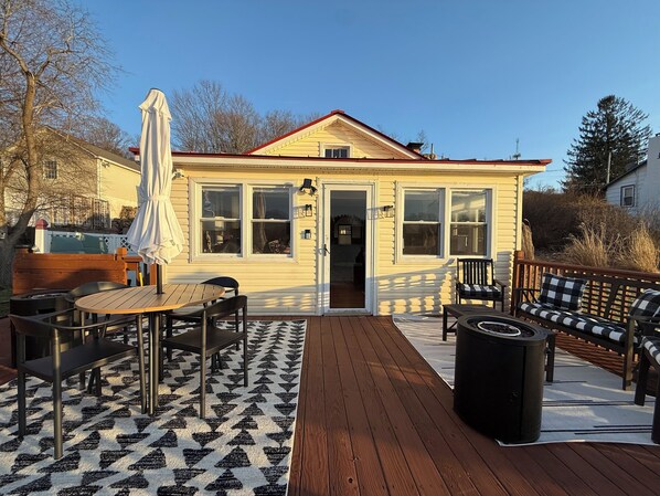 A deck with outdoor furniture, a covered patio area, and a house with large windows. - Cozy Cottage on the Lake (Port Jervis)