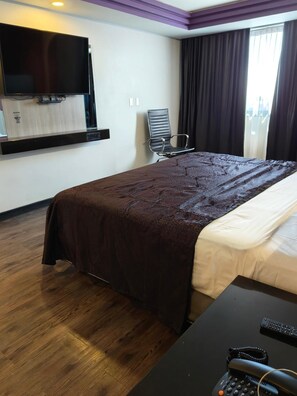 A hotel room with a bed, a desk with a telephone, a chair, a television mounted on the wall, and a window with curtains. - Maxintimo Hotel (Mexico City)