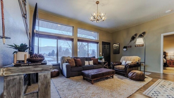 A living room with a sofa, ottoman, and a large window.
