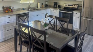 Una cocina moderna con armarios blancos, electrodomésticos de acero inoxidable y un comedor con mesa de vidrio y sillas oscuras.