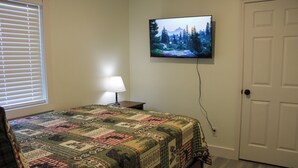 Un dormitorio con cama, televisor montado en la pared, una puerta y ventana con persianas.
