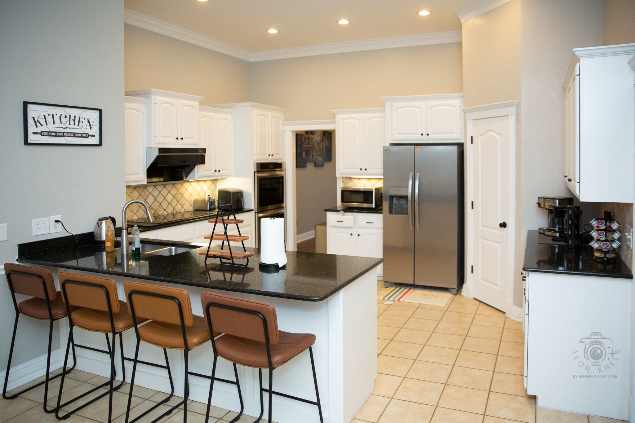 A modern kitchen with white cabinets, a stainless steel refrigerator, and a central island with bar stools.
