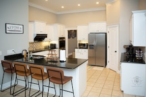 A modern kitchen with white cabinets, a stainless steel refrigerator, and a central island with bar stools.