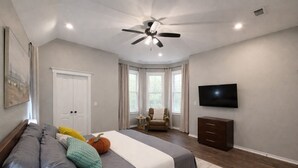 A bedroom with a bed, a ceiling fan, a TV, a chair, and a window. -  11-Acre fenced 3500 SqFt Ranch on I-30, 2 King Suites, 1 Story. 10 Beds. Pond. (Mount Pleasant)