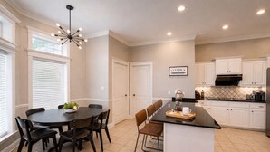 A modern kitchen with a central island, white cabinetry, and a dining area with a round table and chairs. -  11-Acre fenced 3500 SqFt Ranch on I-30, 2 King Suites, 1 Story. 10 Beds. Pond. (Mount Pleasant)