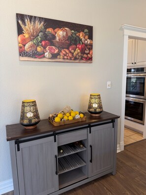 Una cocina con un armario de madera, dos lámparas, una cesta de frutas y un cuadro en la pared.