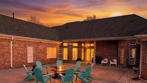 A brick building with a fire pit and chairs in the center, surrounded by a covered patio area. -  11-Acre fenced 3500 SqFt Ranch on I-30, 2 King Suites, 1 Story. 10 Beds. Pond. (Mount Pleasant)