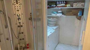 Ein kleines Badezimmer mit Dusche, einer Waschmaschine und einem Ablagefach für Toilettenartikel.