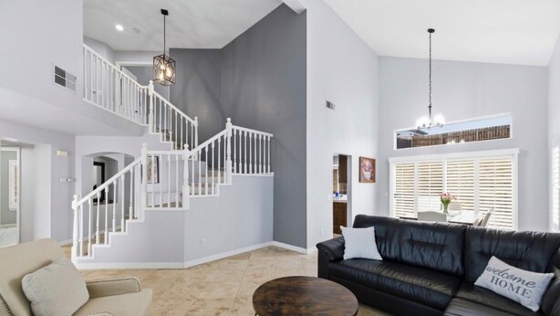 Un vaste espace de vie comprenant un escalier, un canapé en cuir noir, une table basse ronde et une vue sur l’extérieur grâce à une fenêtre munie de stores.